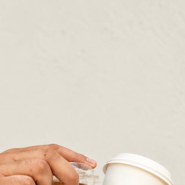 Mano sosteniendo un vaso frío y un vaso caliente contra una pared clara