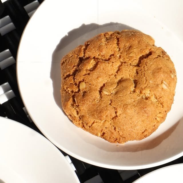 Galleta grande de avena dorada en plato blanco sobre mesa tejida