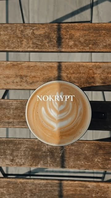 Latte con arte de hoja y la palabra NOKRYPT sobre una mesa de madera, vista desde arriba
