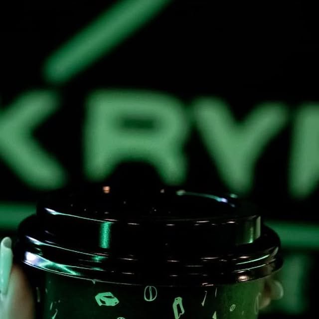 Vaso para llevar negro y verde frente al letrero de neón de Nokrypt
