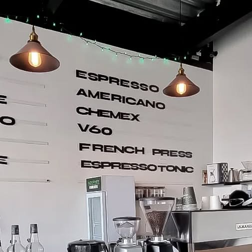El muro real de Nokrypt: ESPRESSO, AMERICANO, CHEMEX, V60, FRENCH PRESS y ESPRESSOTONIC en letras negras sobre la barra